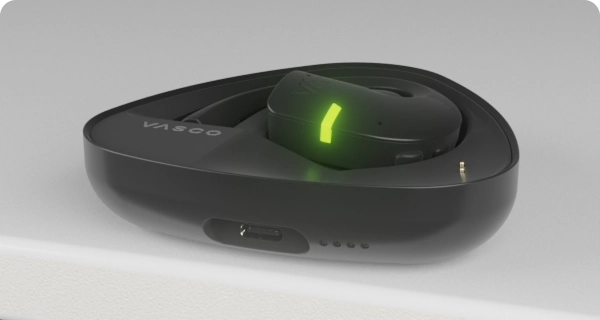 A Vasco Translator E1 earbud is placed inside its charging case. The flashing LED indicators show the current battery level of the case and earbud. 