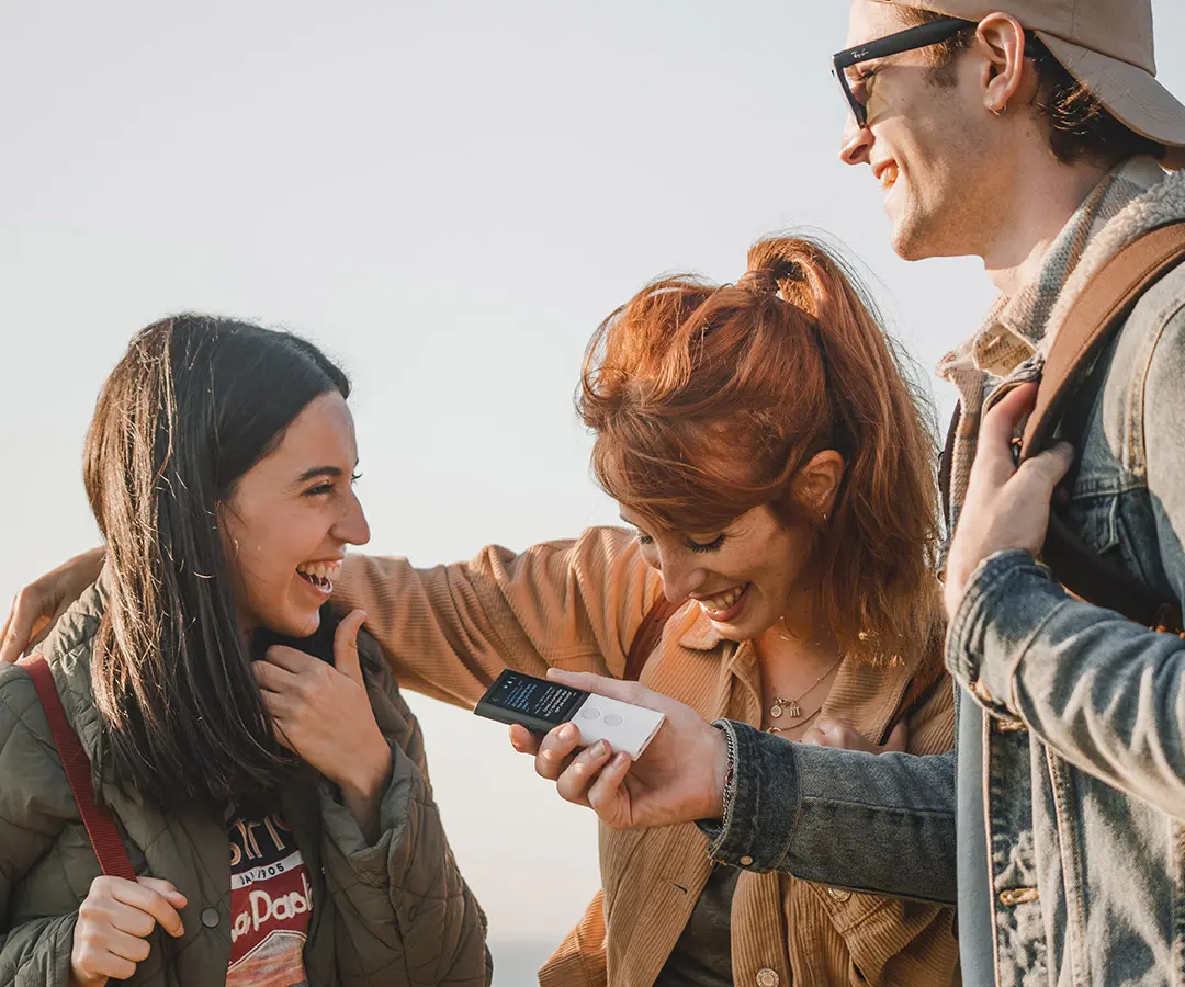 Three young friends laughing and chatting using a translator, enjoying a fun moment together. 