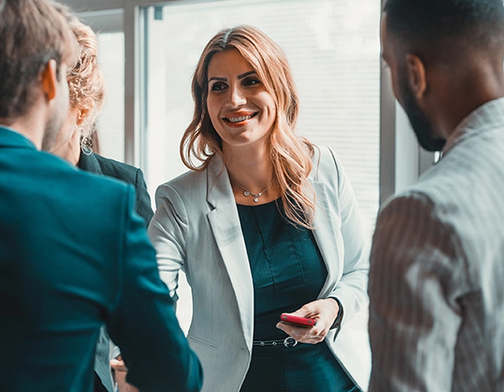 A woman holding a Vasco Translator V4 in her hand, shaking hands with another person in an office setting.