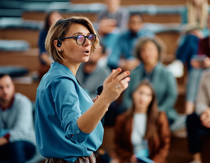 A woman giving a speech at a university, wearing a Vasco Translator E1 in her ear.