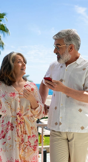 Two elderly people holding Vasco V4 devices, talking to each other, demonstrating five different playback speed options.