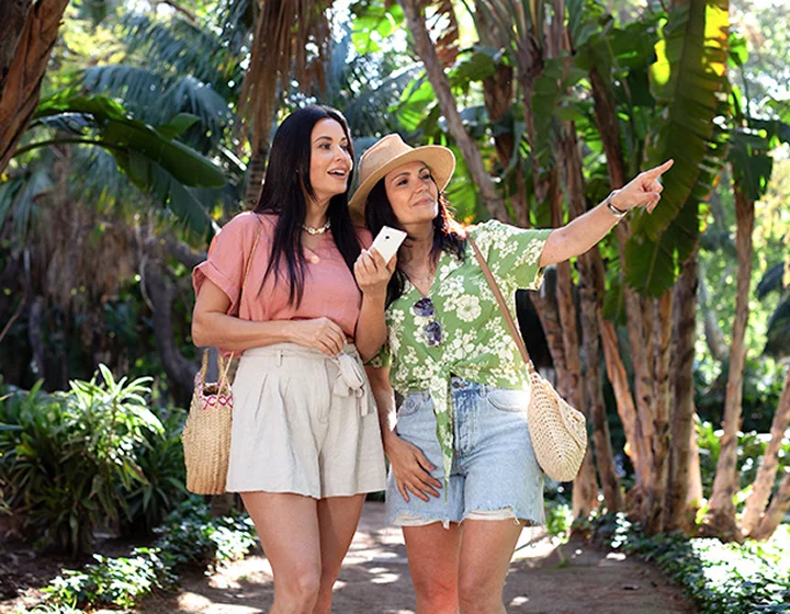 Two women in a vacation setting looking in the direction one of them is pointing. One woman is holding a Vasco Translator V4 in her hand.