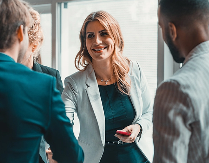 A woman holding a Vasco Translator V4 in her hand, shaking hands with another person in an office setting.