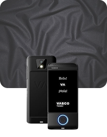 A product showcase image featuring a black Vasco Translator device from two angles against a dark, textured fabric background. The device on the left shows the back view, highlighting a camera lens with a flash and an embossed 
