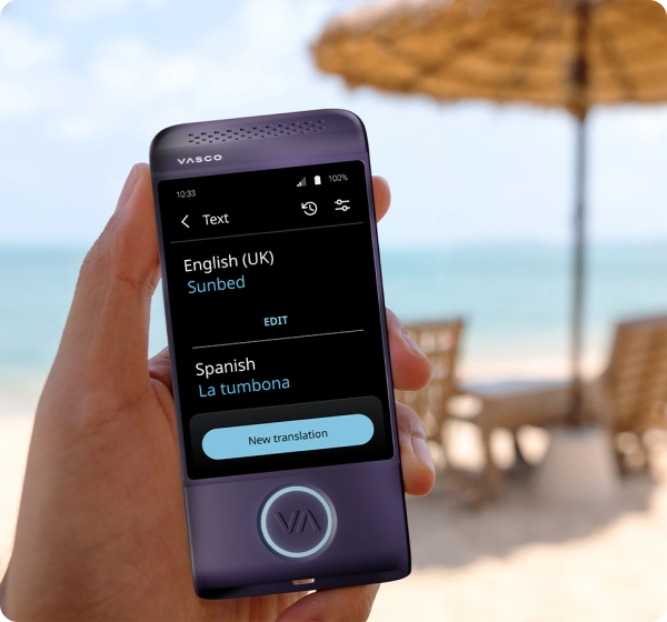 A close-up shot of a hand holding a purple Vasco electronic translator device. The screen displays a text translation from English (UK) to Spanish, showing the word 