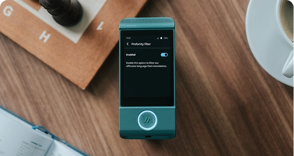 A top-down shot of a teal Vasco electronic translator resting on a wooden table. The device's screen is active, showing the 