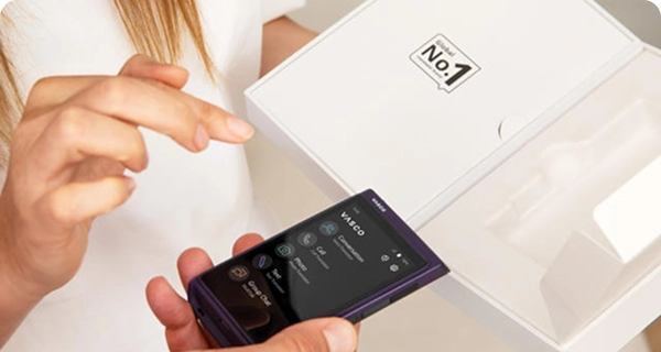 A close-up of a person unboxing a purple Vasco Translator Q1 from its white retail box.