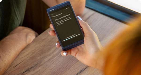 An over-the-shoulder view of a woman holding a blue Vasco Translator Q1 over a wooden table inside a train. The device screen displays a 'Software update' notification with a progress bar indicating 'Downloading update...'.